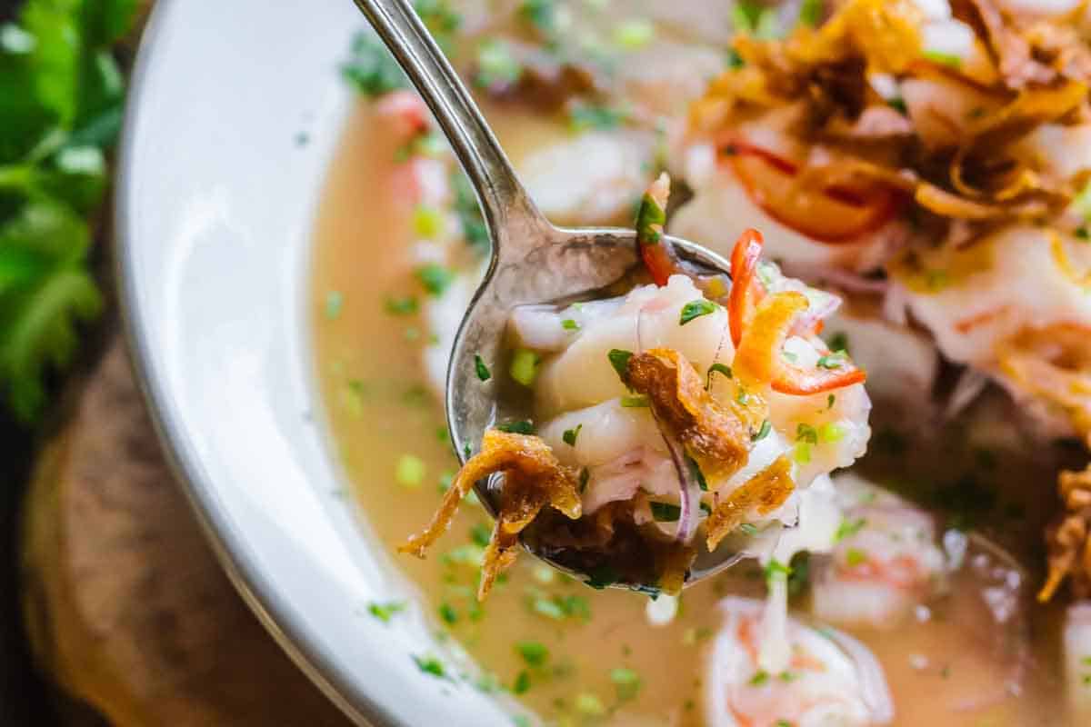 A spoon of shrimp ceviche over a soup bowl.