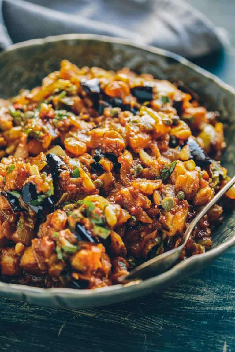 A serving bowl of caponata with raisins and pine nuts.