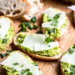 Several pieces of Fava bean crostini on a wooden board.