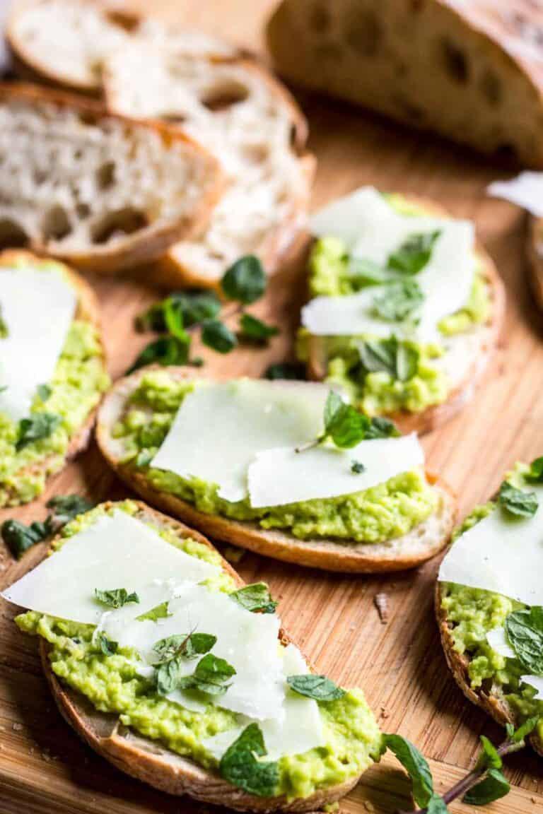 Several pieces of Fava bean crostini on a wooden board.