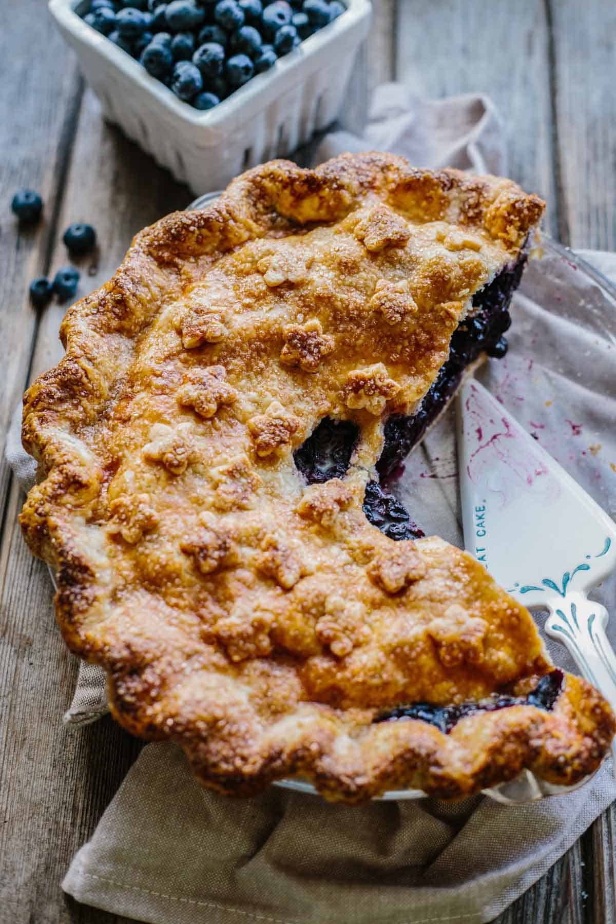 A blueberry pie in a pie plate with one fourth missing.