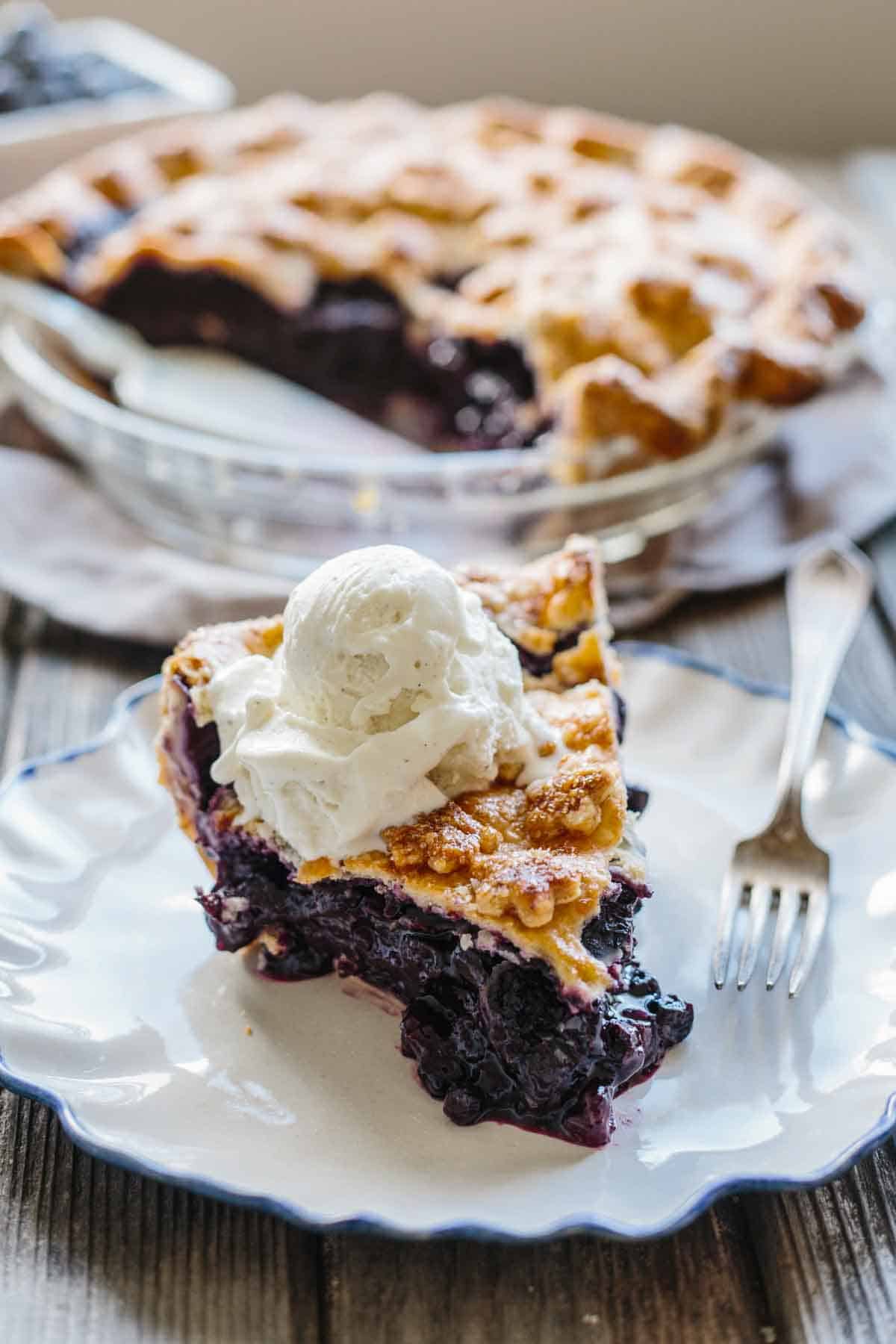 Slice of blueberry pie a la mode on a dessert plate with a fork.