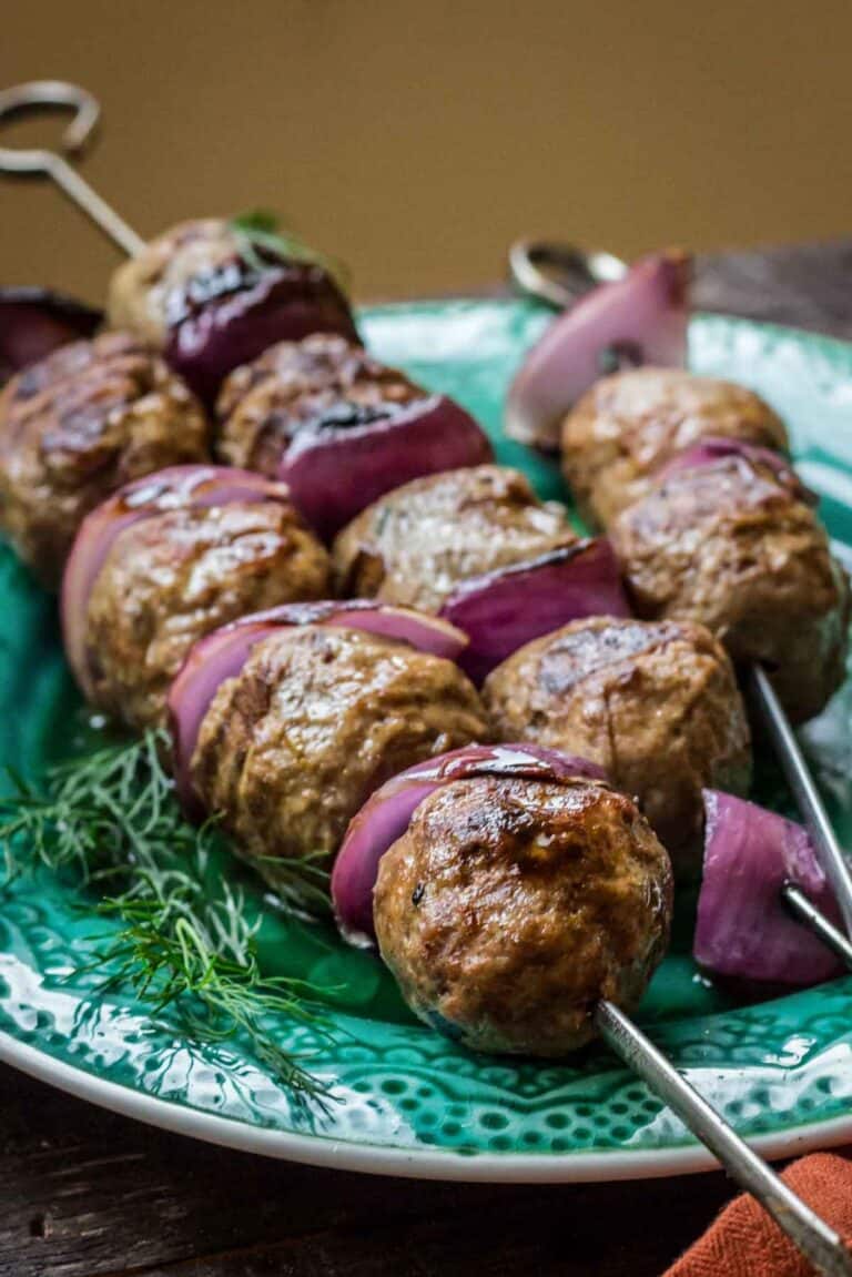 Lamb meatballs and red onion slices on metal skewers on a green plate.