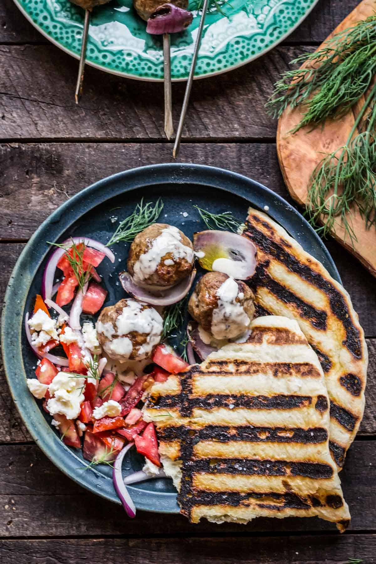 A large blue dinner plate with grilled pita, lamb meatballs, and tahini.