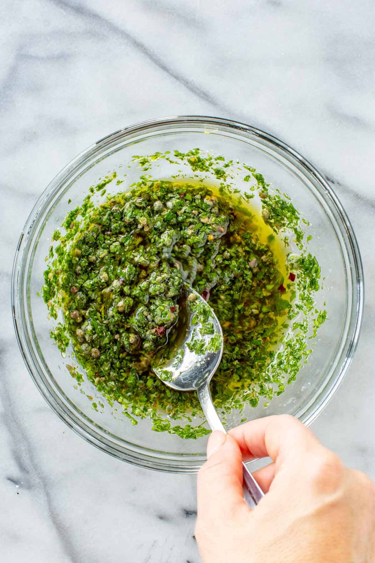 Mixing together herbs, olive oil, capers and anchovies in a bowl.