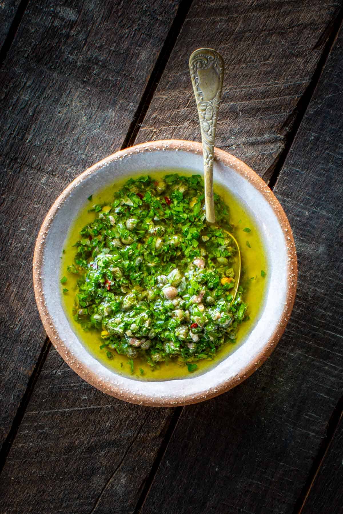 Italian salsa verde in a small bowl with a spoon on a dark wooden board.