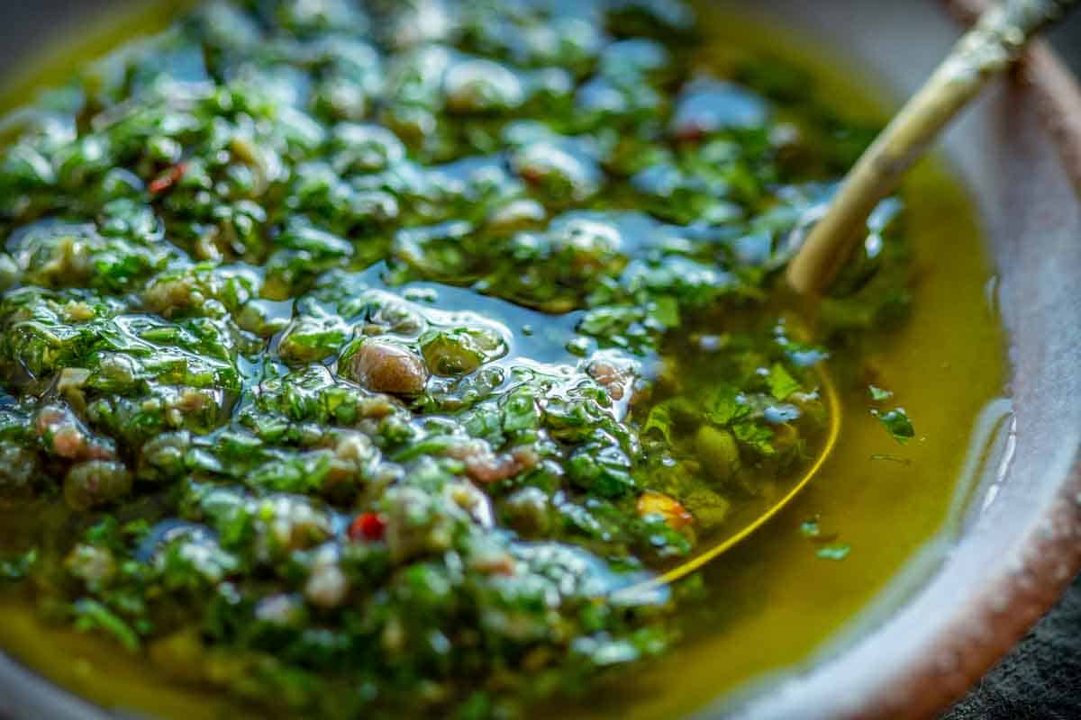 Close up of a spoon in a mixture of herbs and olive oil.