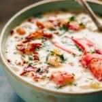 A pale green bowl of lobster chowder with a piece lobster claw meat.