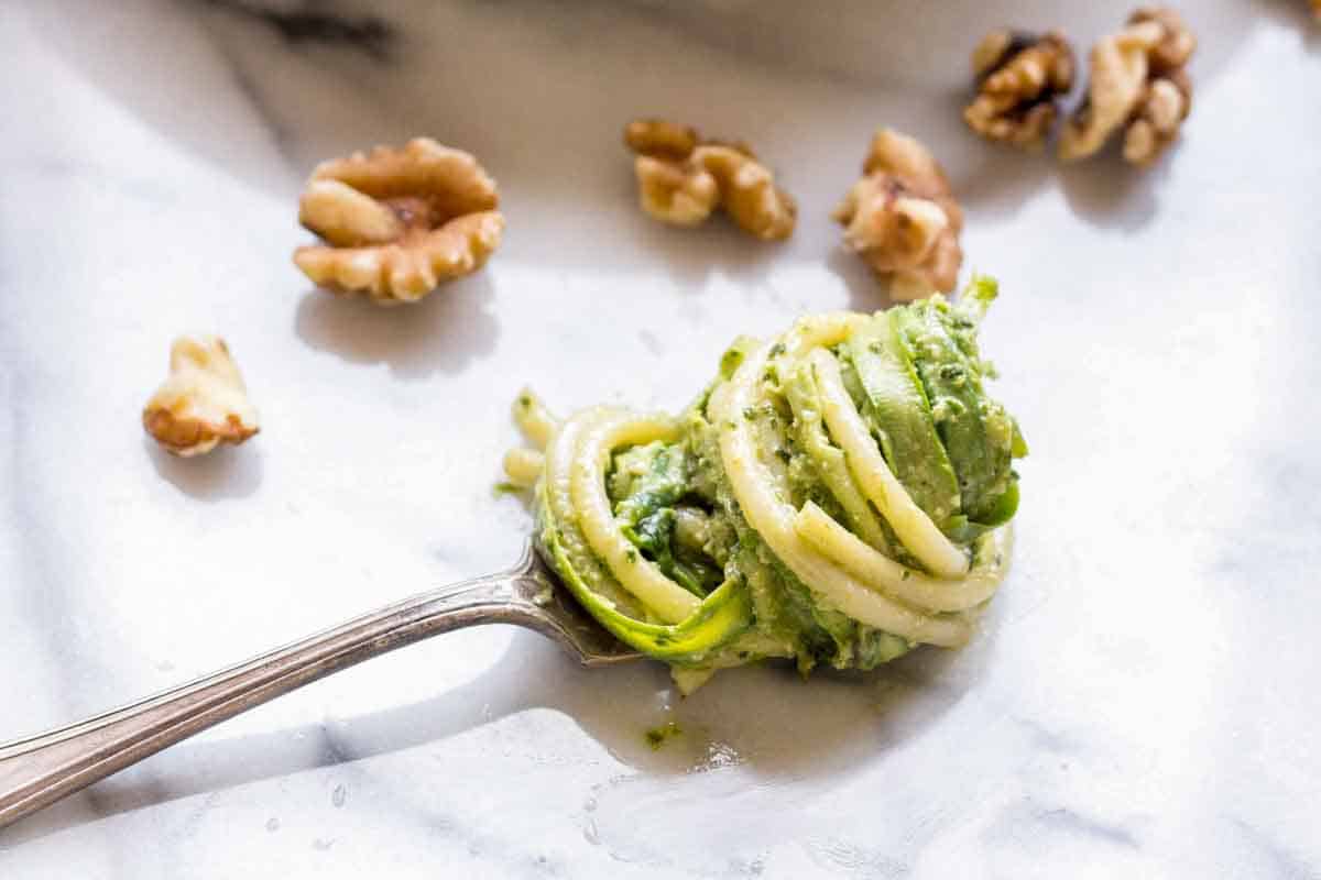 Spaghetti twirled on a fork next to walnuts on a marble counter.