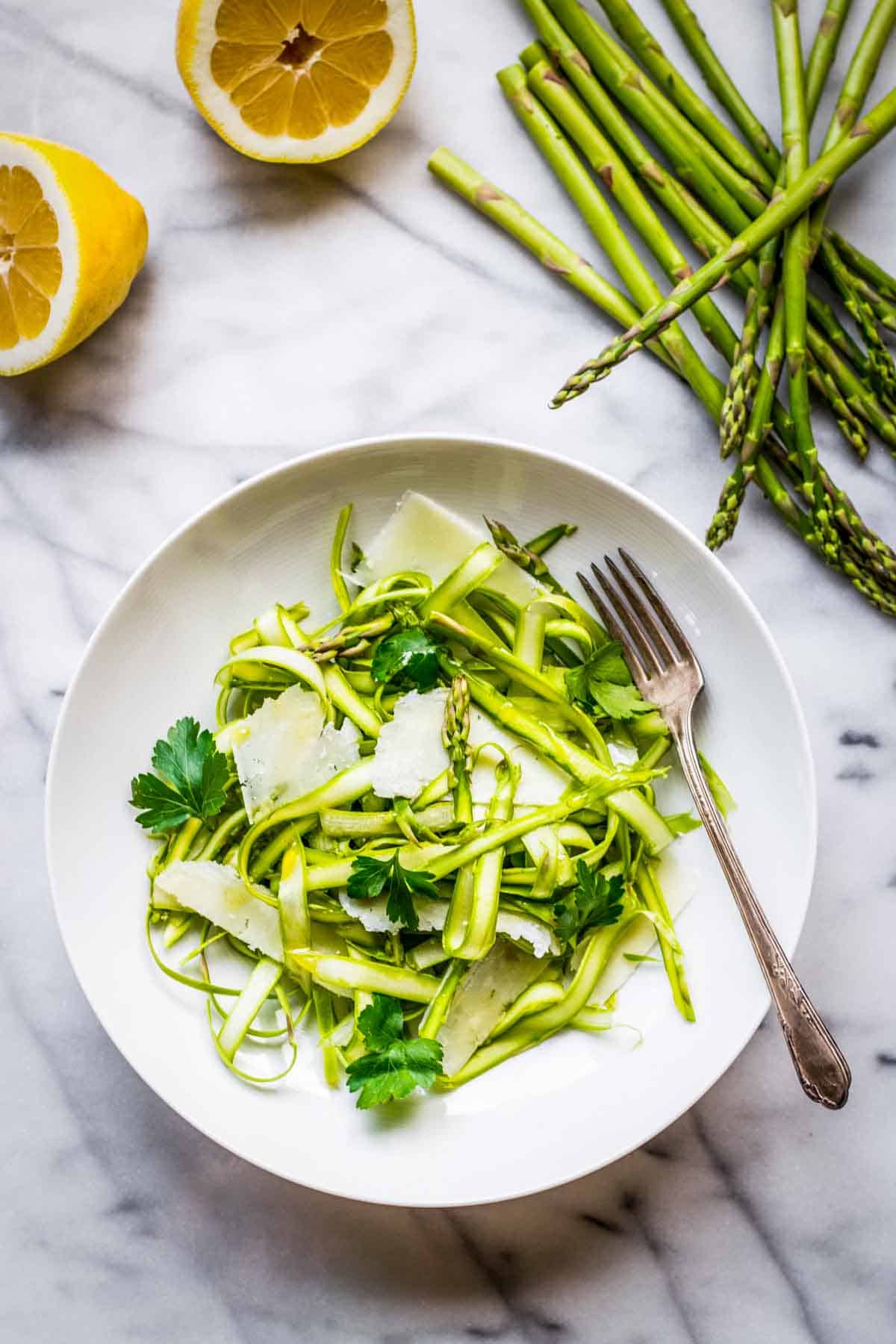 A white plate with raw asparagus salad and whole ingredients in the background.