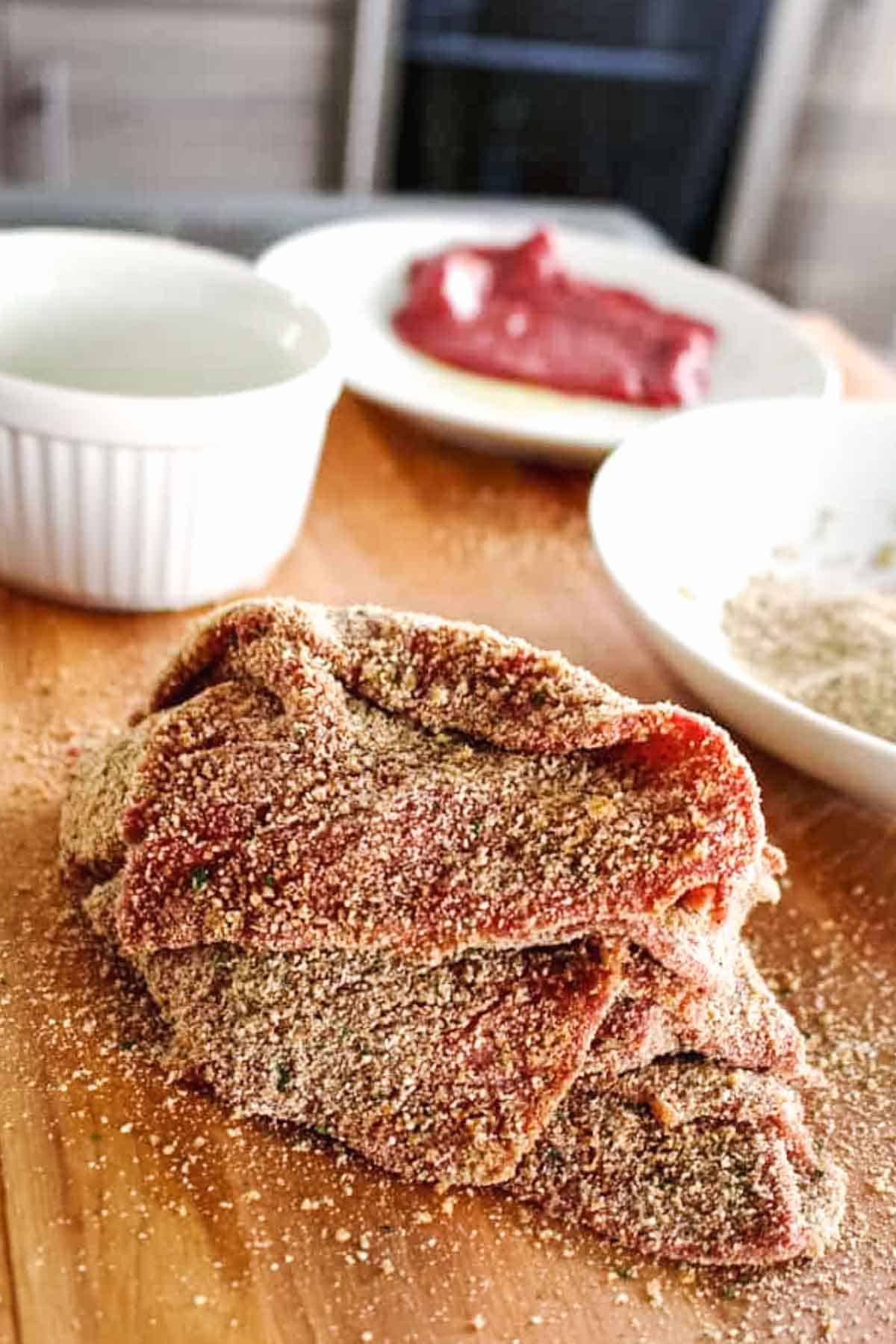 A pile of breaded thin slices of beef in front of the breading station.