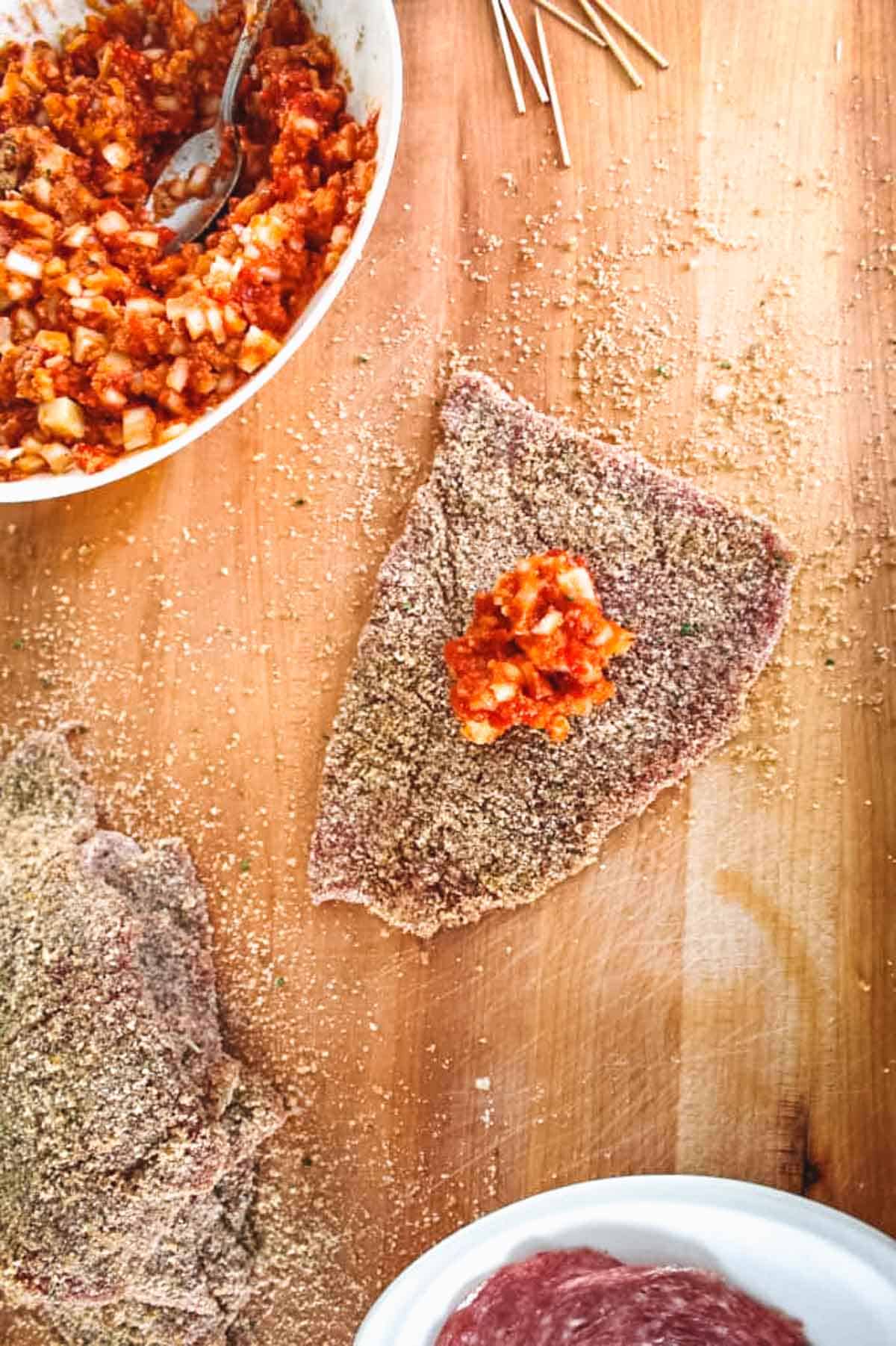 A piece of thinly sliced breaded beef with a tomato cheese mixture dolloped in the center.