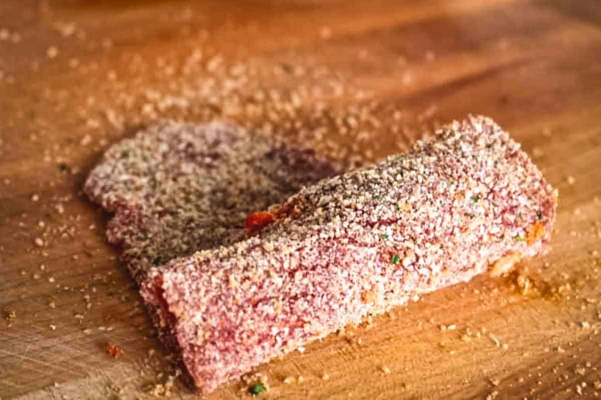 A thin breaded beef cutlet being rolled up.
