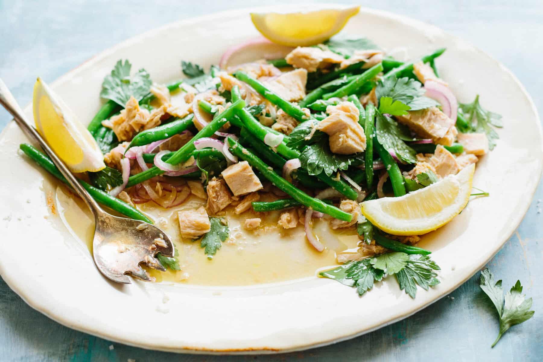 A platter half full of Italian tuna salad with green beans, lemon and parsley.