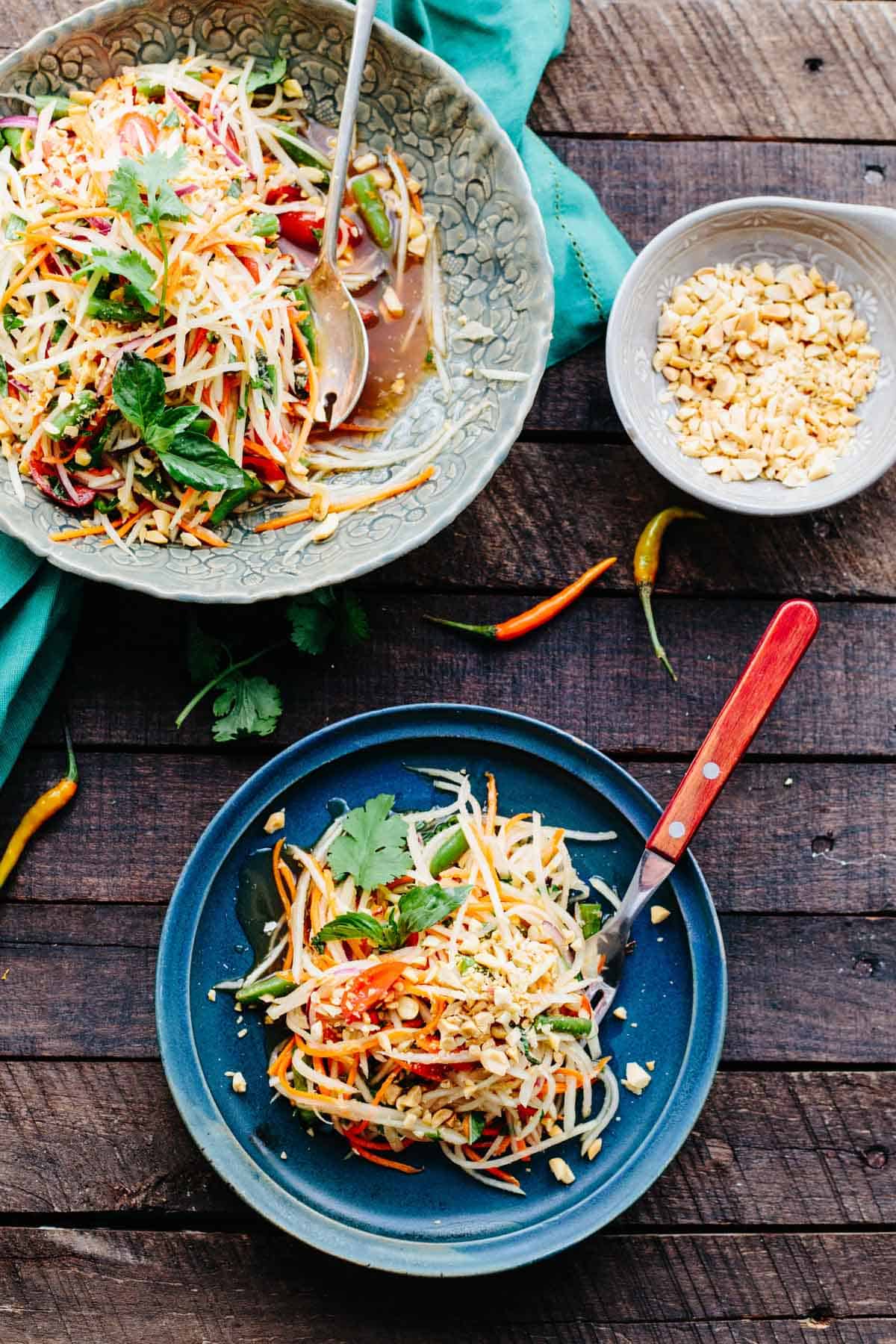 A tables cape with plates and bowls of green papaya salad with peanuts.