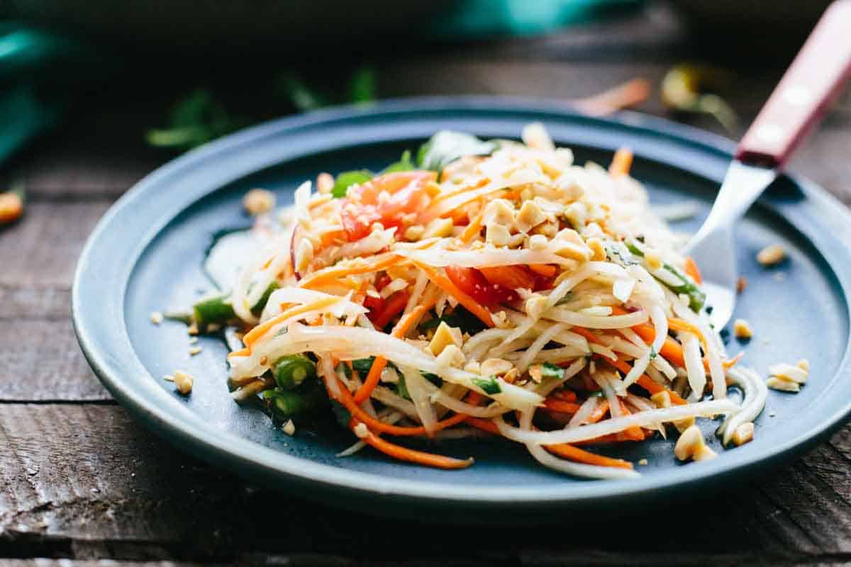 Julienned vegetables on a plate with herbs and chopped peanuts on top.