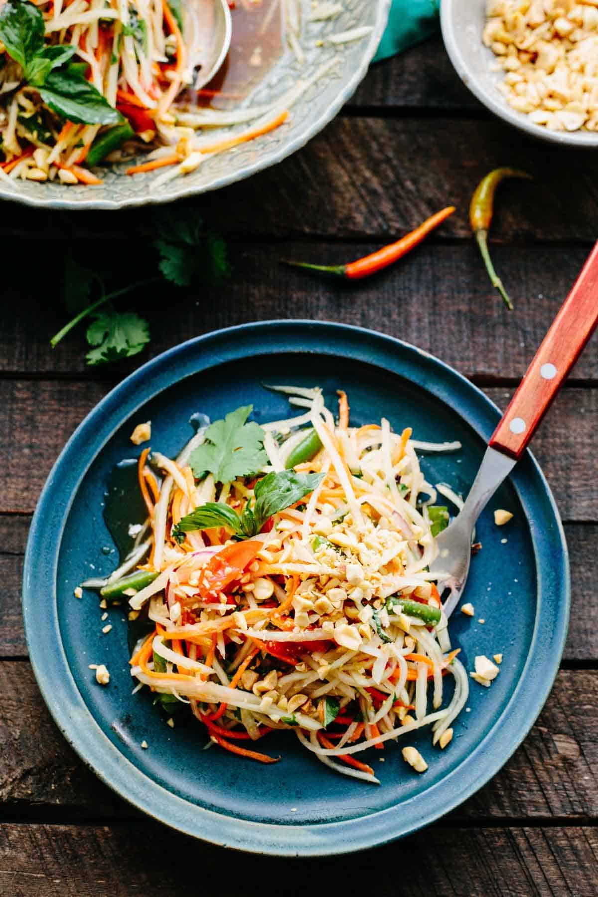 A blue plate with Thai green papaya salad and a fork.