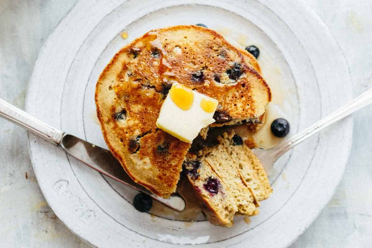 Pancakes with a pat of butter on a plate with a piece taken out.