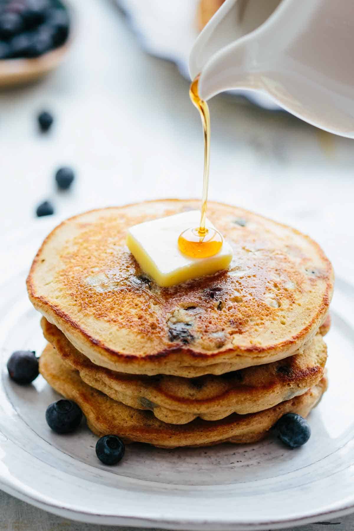 A stack of pancakes with a pat of butter and syrup being drizzled over top.