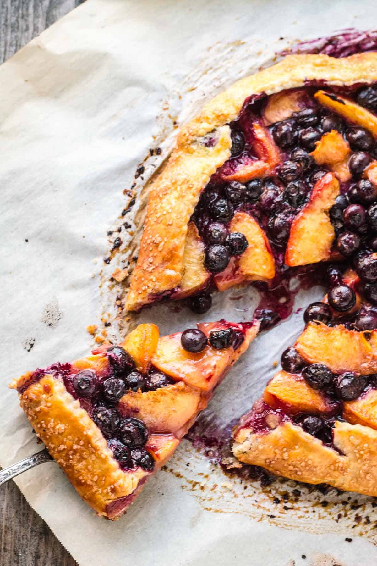 A slice being removed from a free form blueberry peach tart.