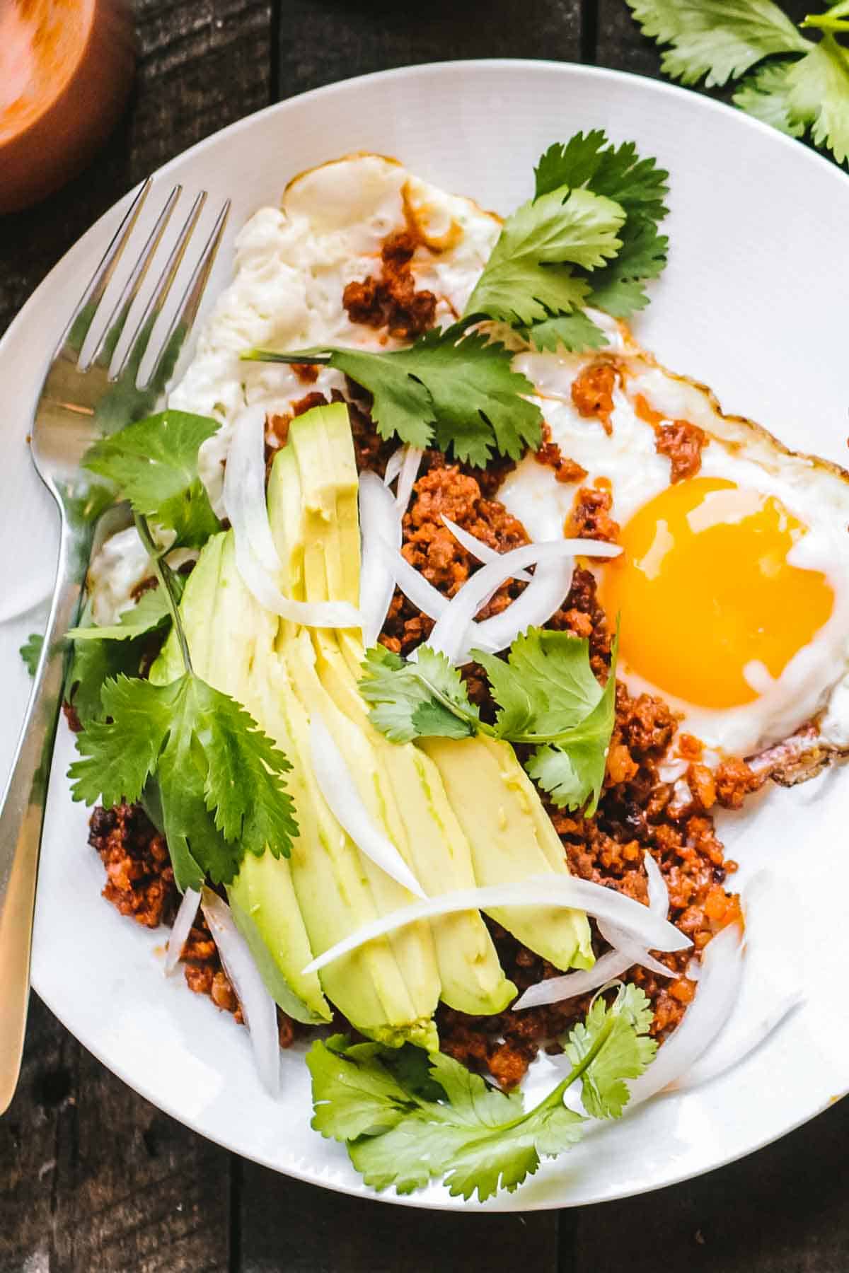 A white plate with fried eggs, chorizo and avocado on top with a fork.