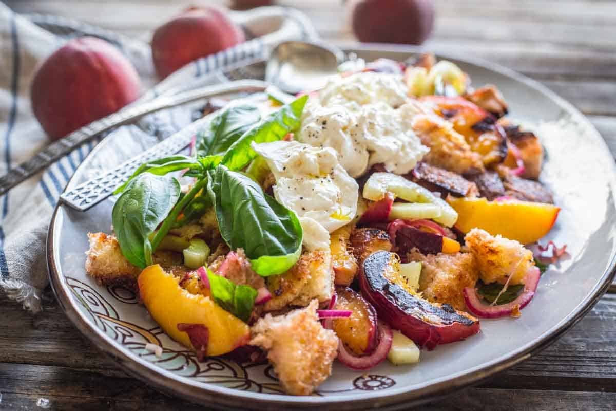 A large platter of peach and bread salad with cheese and basil on top.