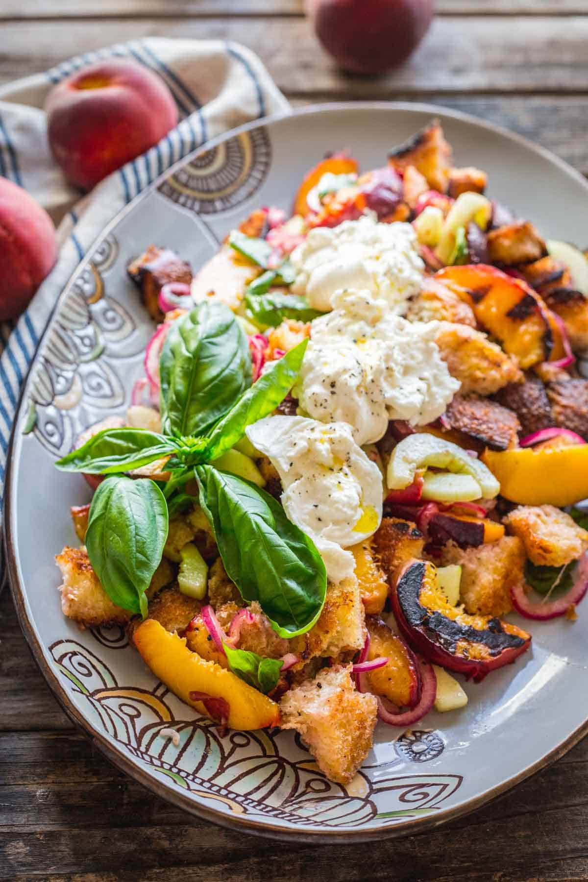 A large platter of peach panzanella with burrata and a big sprig of basil.