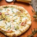 A grilled pizza with a pizza cutter and a sprig of fresh herbs.