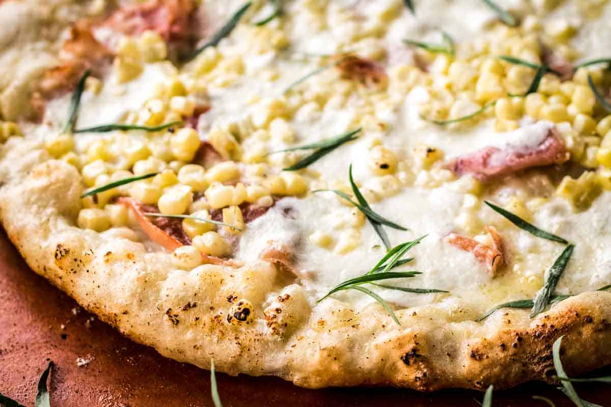 Corn, prosciutto, cheese and fresh herbs on a charred pizza crust.