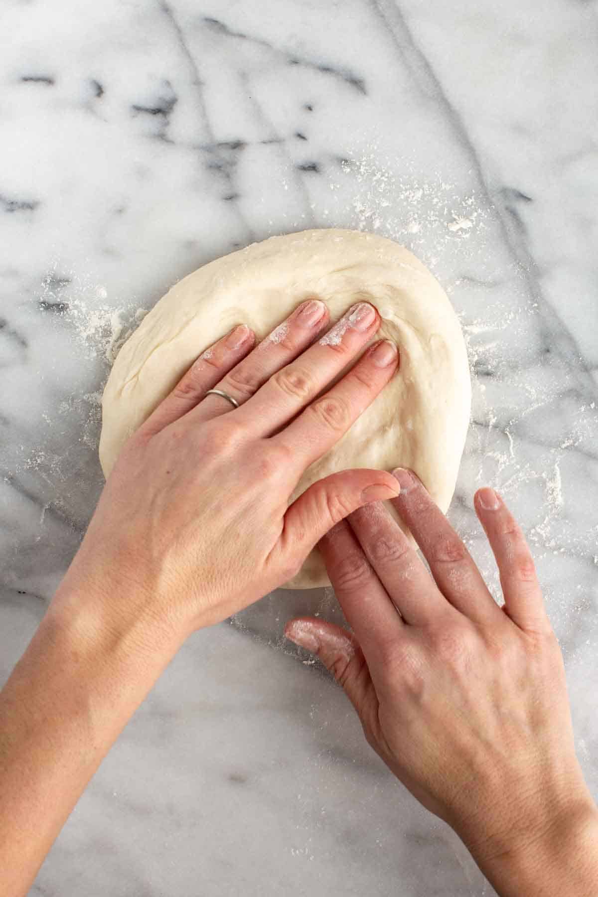 Hands working a ball of pizza dough on a marble counter. 