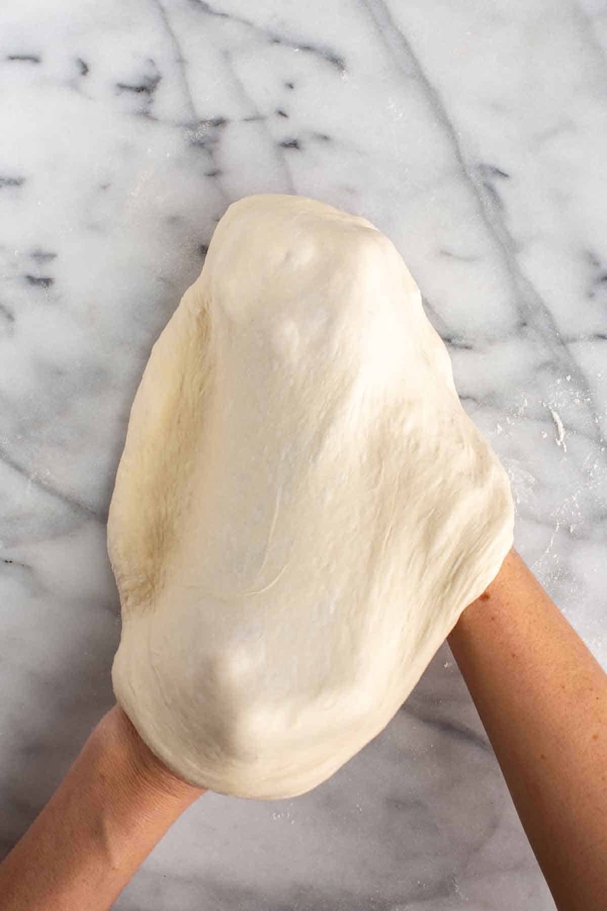 Hands stretching a ball of pizza dough.