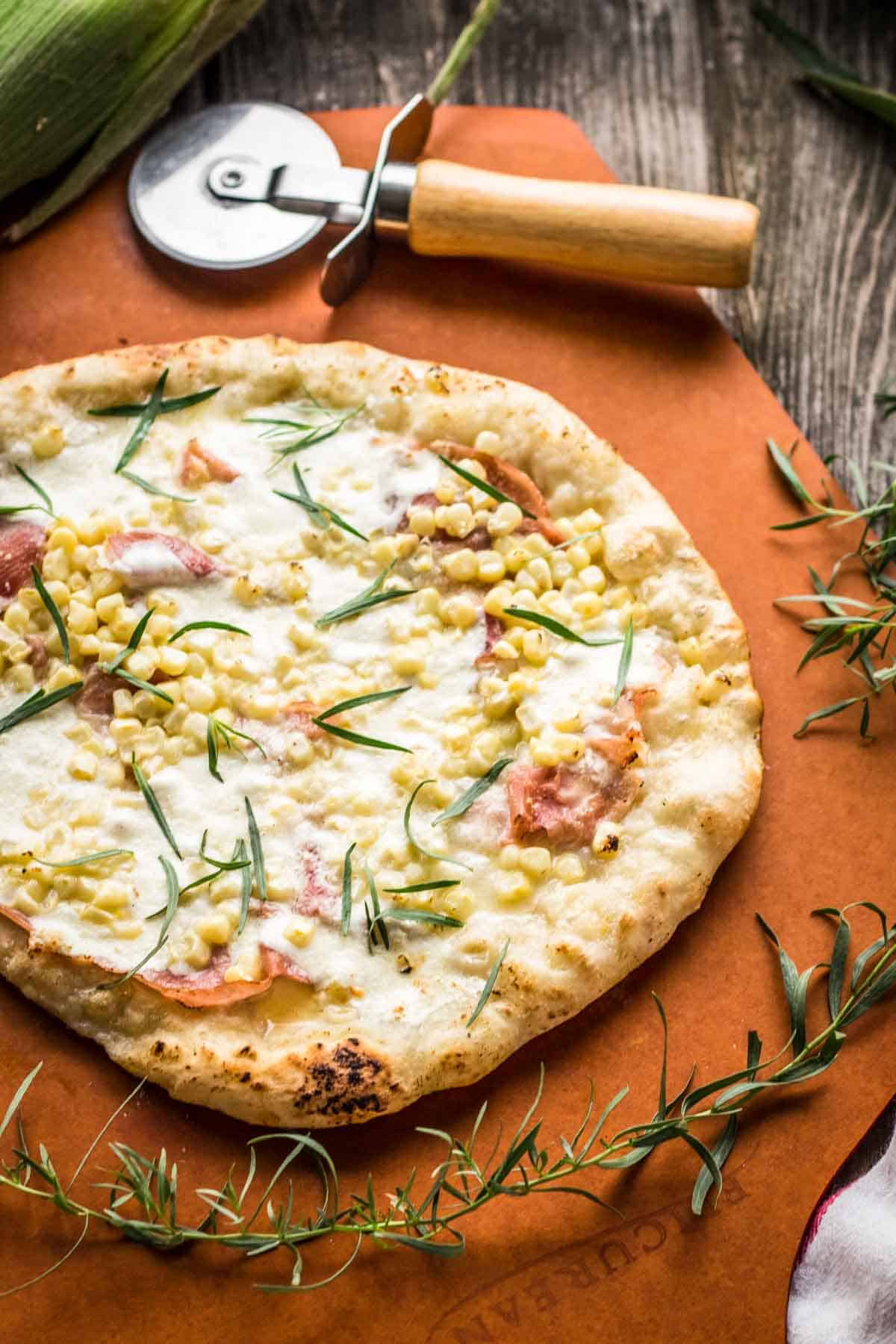 A grilled pizza with a pizza cutter and a sprig of fresh herbs.