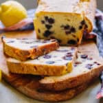 Three slices of lemon blueberry pound cake cut off a loaf on a wood cutting board.