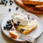 A fork cutting a bite off a slice of lemon blueberry pound cake on a small plate.