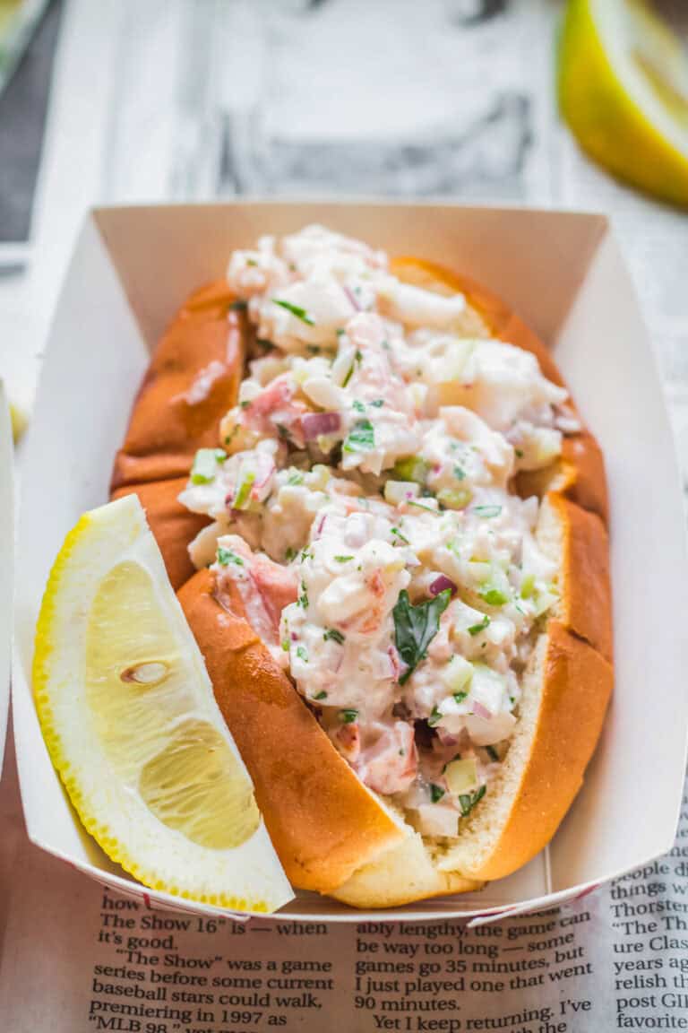 Maine lobster roll in a paper boat with a lemon wedge.
