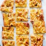 A whole focaccia cut into pieces with thinly sliced lemon and rosemary ont op.