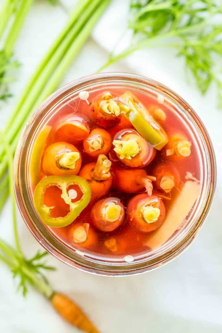 Carrot tops and sliced ginger in a jar in brine.