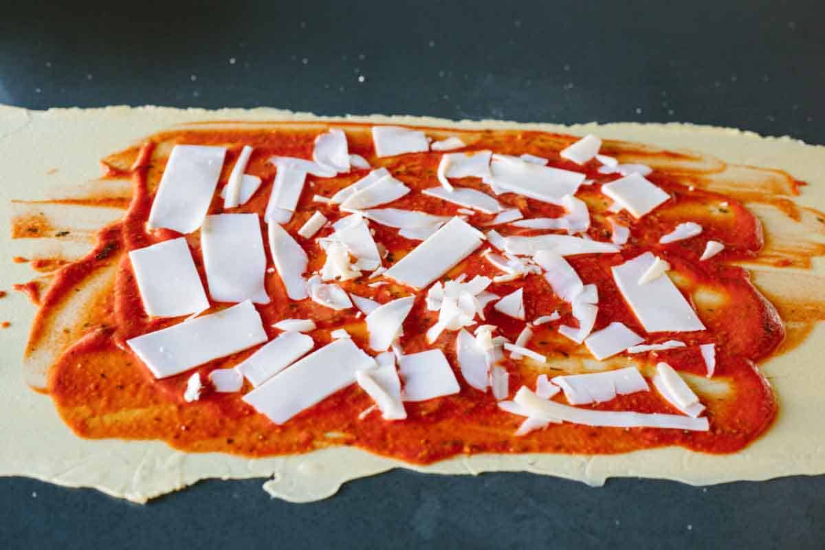 A thinly rolled out sheet of dough with tomato sauce and cheese on top.