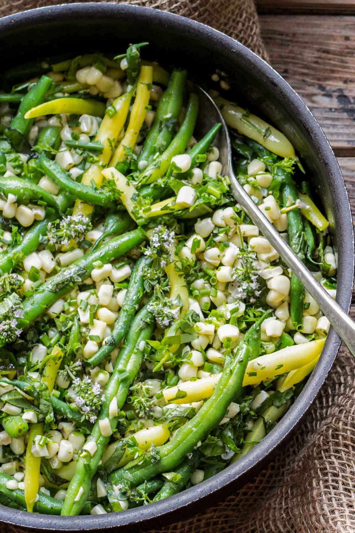 Green beans and corn in a pan with fresh herbs and a serving spoon. 
