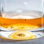 Close up of apple cider vinegar in a glass with trapped fruit flies.
