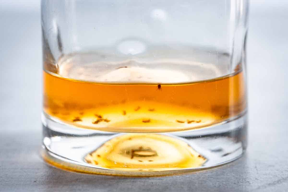 Close up of apple cider vinegar in a glass with trapped fruit flies.