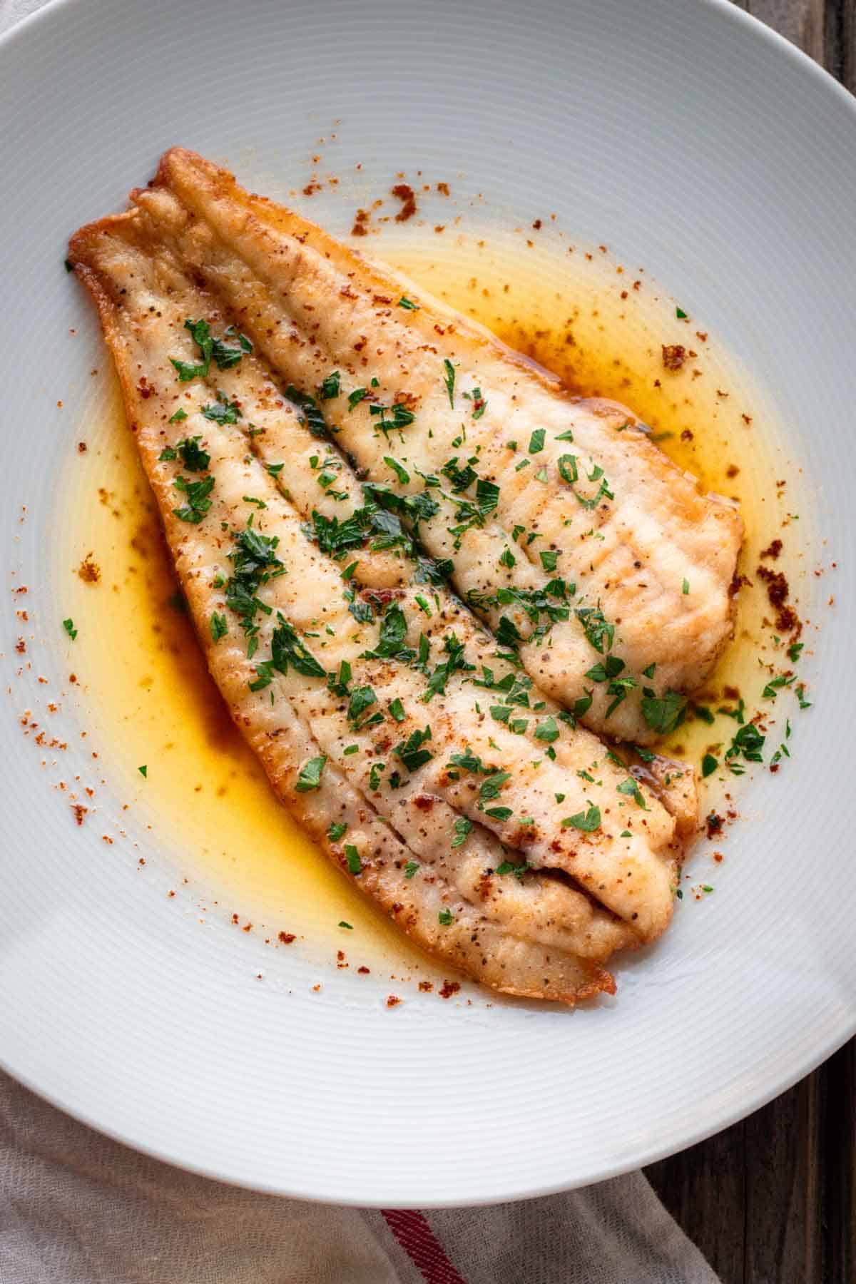 A fillet of white fish in a butter sauce garnished with parsley.