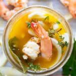 A piece of shrimp and herbs peeking out of a jar of pickle brine.