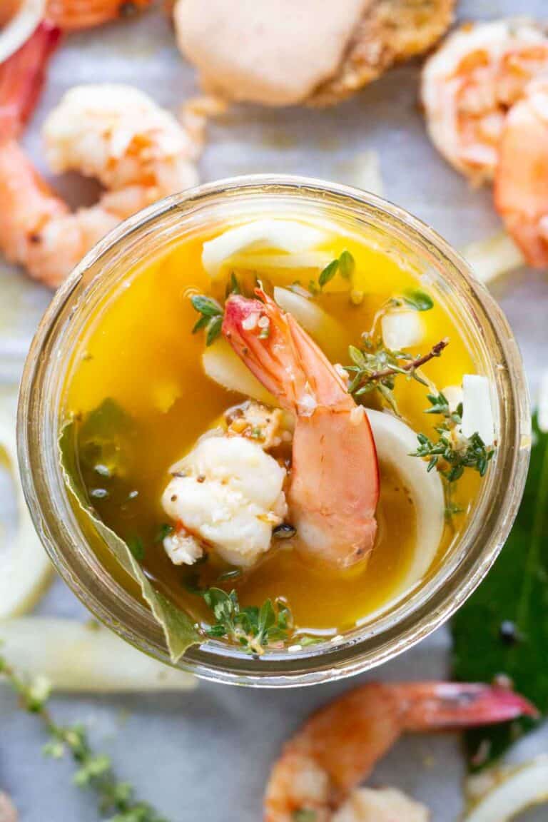 A piece of shrimp and herbs peeking out of a jar of pickle brine.