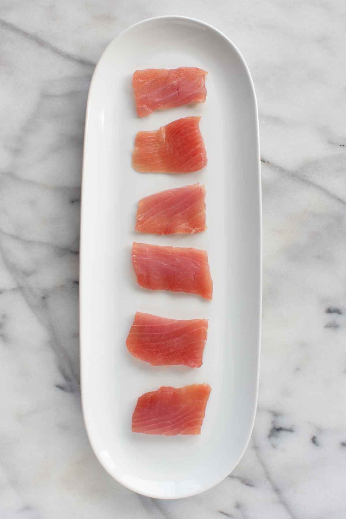 A long white plate with pieces of raw tuna.