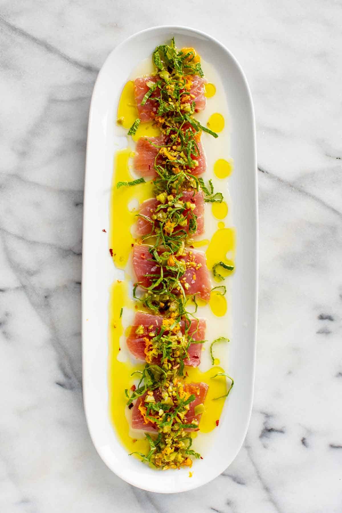 A long white plate with tuna crudo and Sicilian inspired accoutrements.