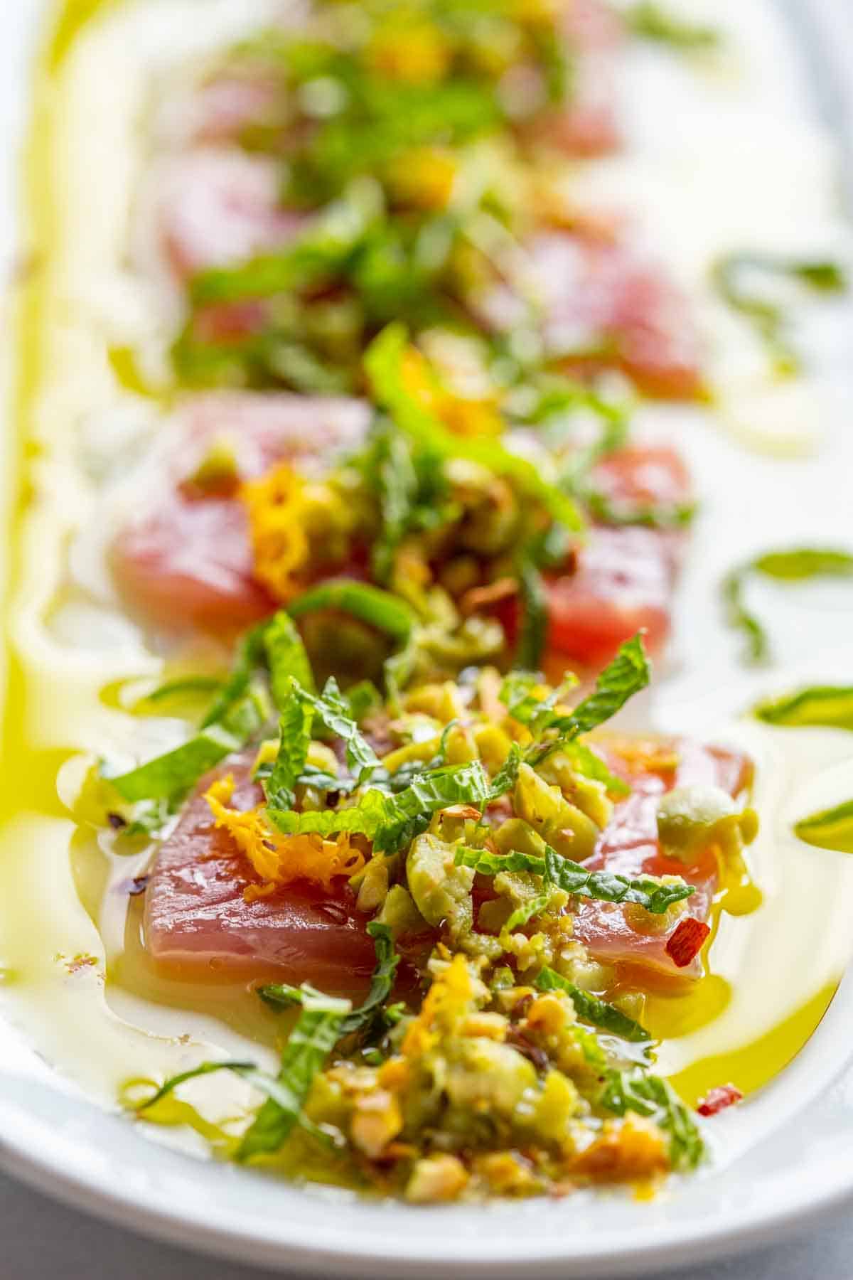 Slices of raw tuna crudo topped with lemon zest, herbs, olives and pistachios.