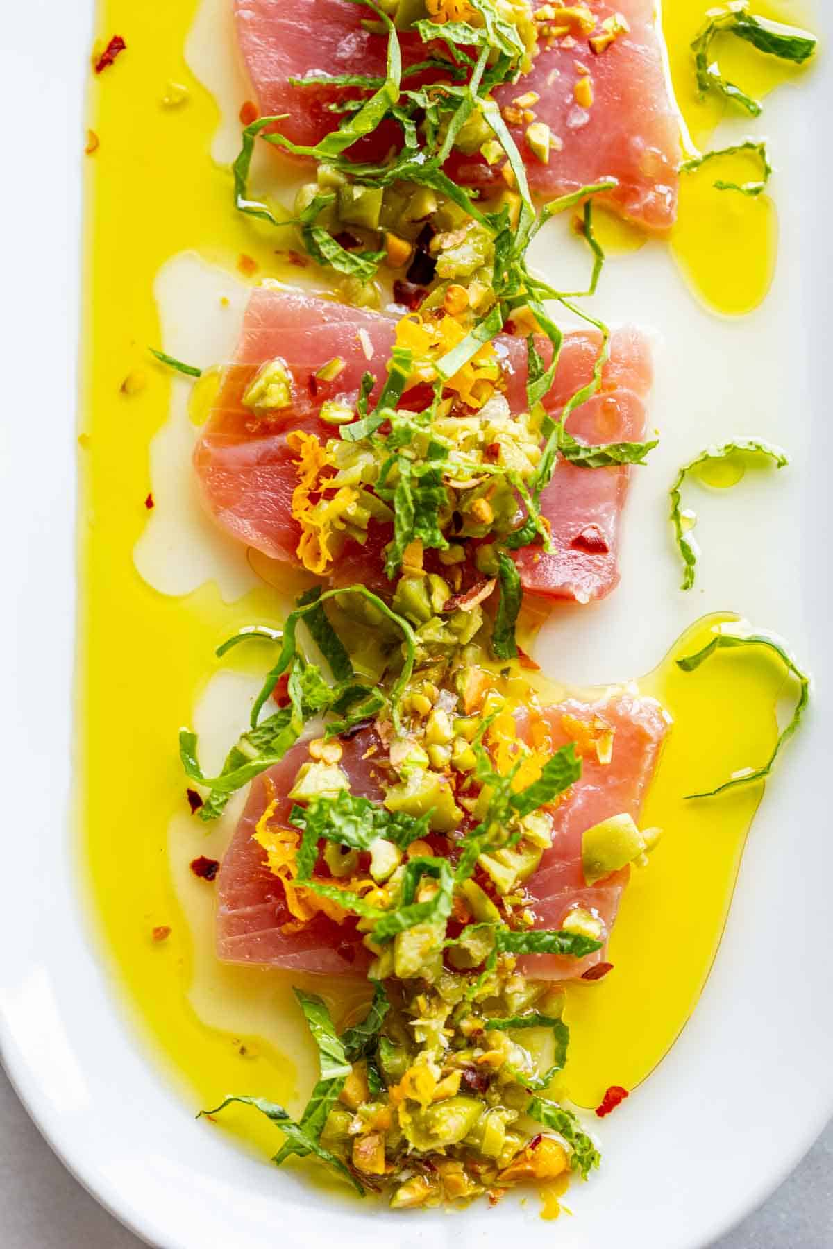 Raw tuna crudo with fresh basil, lemon, nuts and vibrant yellow olives oil.