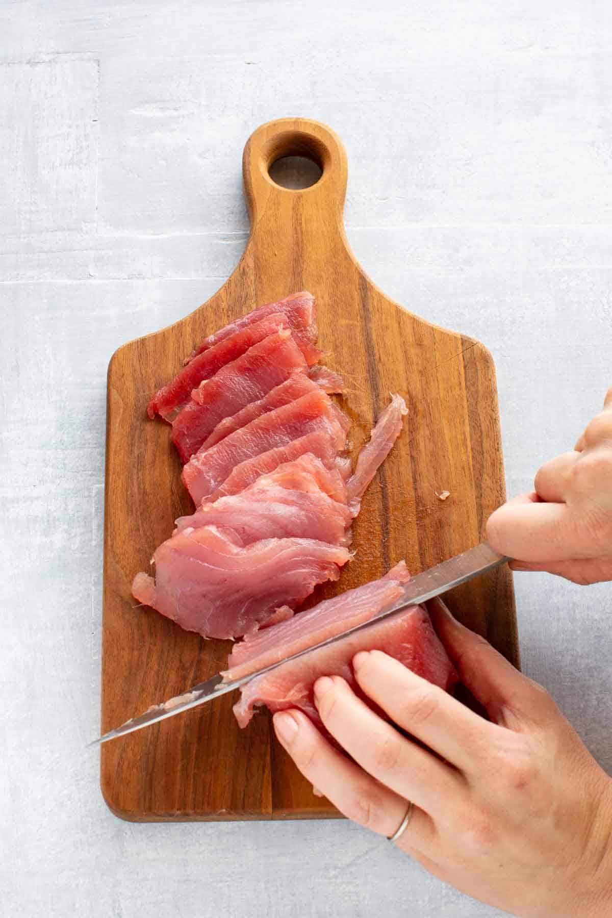 A knife cutting thin slices of raw tuna for crudo.