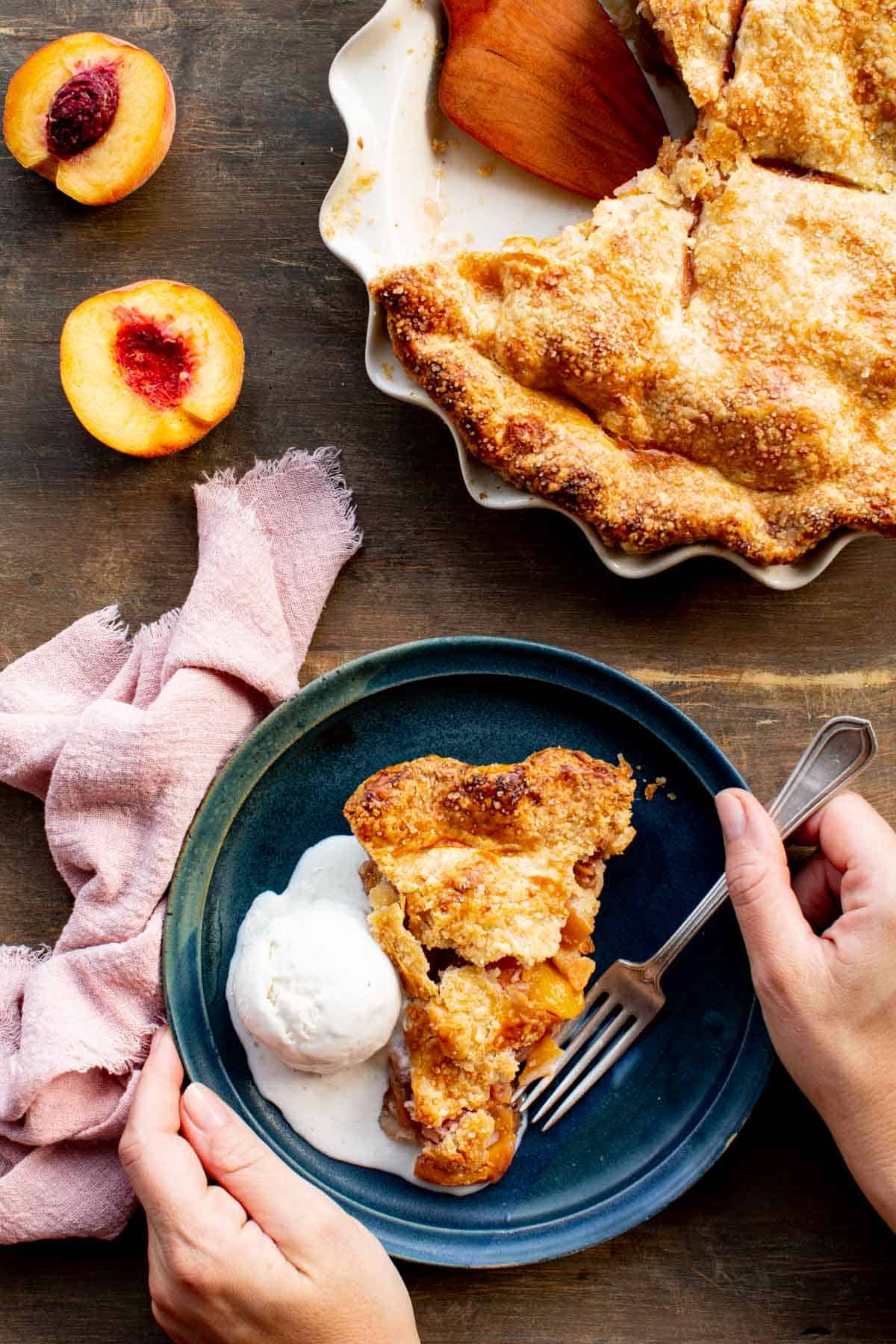 A hand holding a fork with a plate of peach pie with vanilla ice cream.